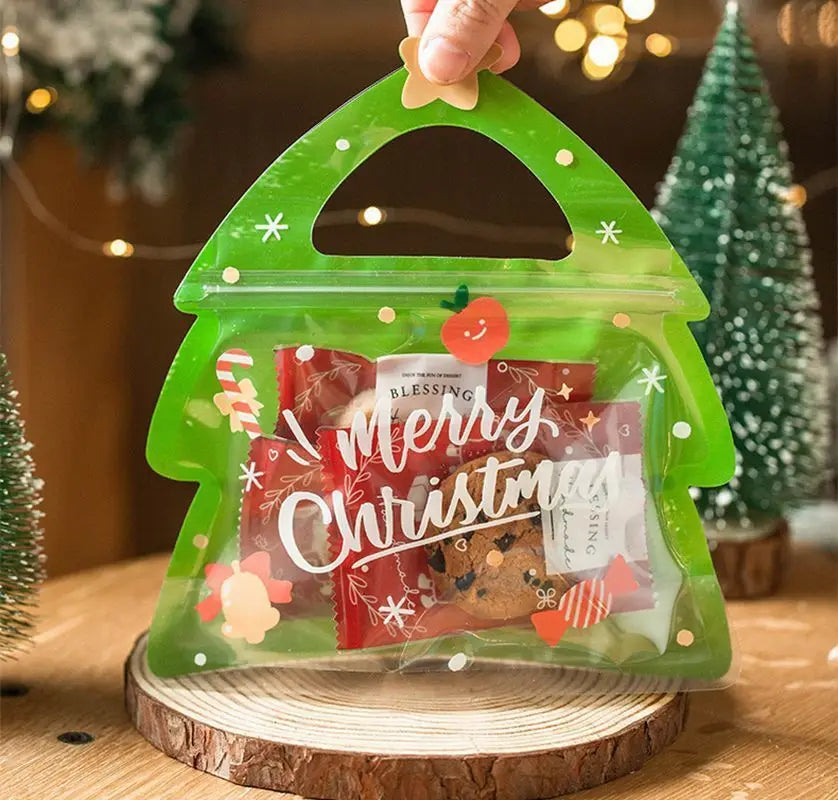 A clear green reusable Christmas gift bag filled with treats and party favors, held by a hand.