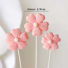 A set of pink felt flower cake toppers with white centers on thin sticks.