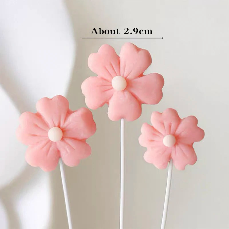 A set of pink felt flower cake toppers with white centers on thin sticks.
