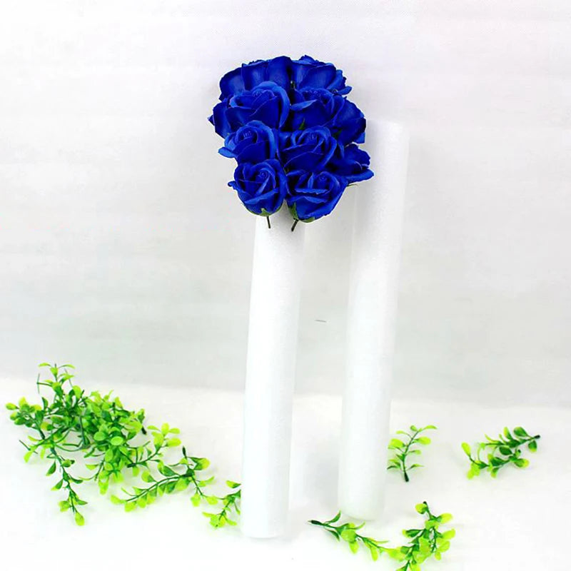 A white foam flower arrangement cylinder with deep blue roses and green foliage.