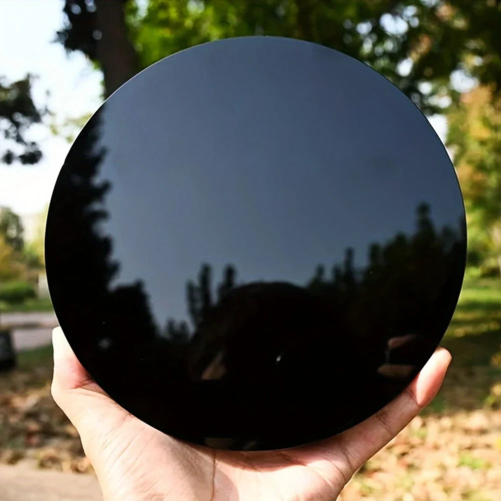 A hand holds a round, black obsidian mirror reflecting surrounding foliage.