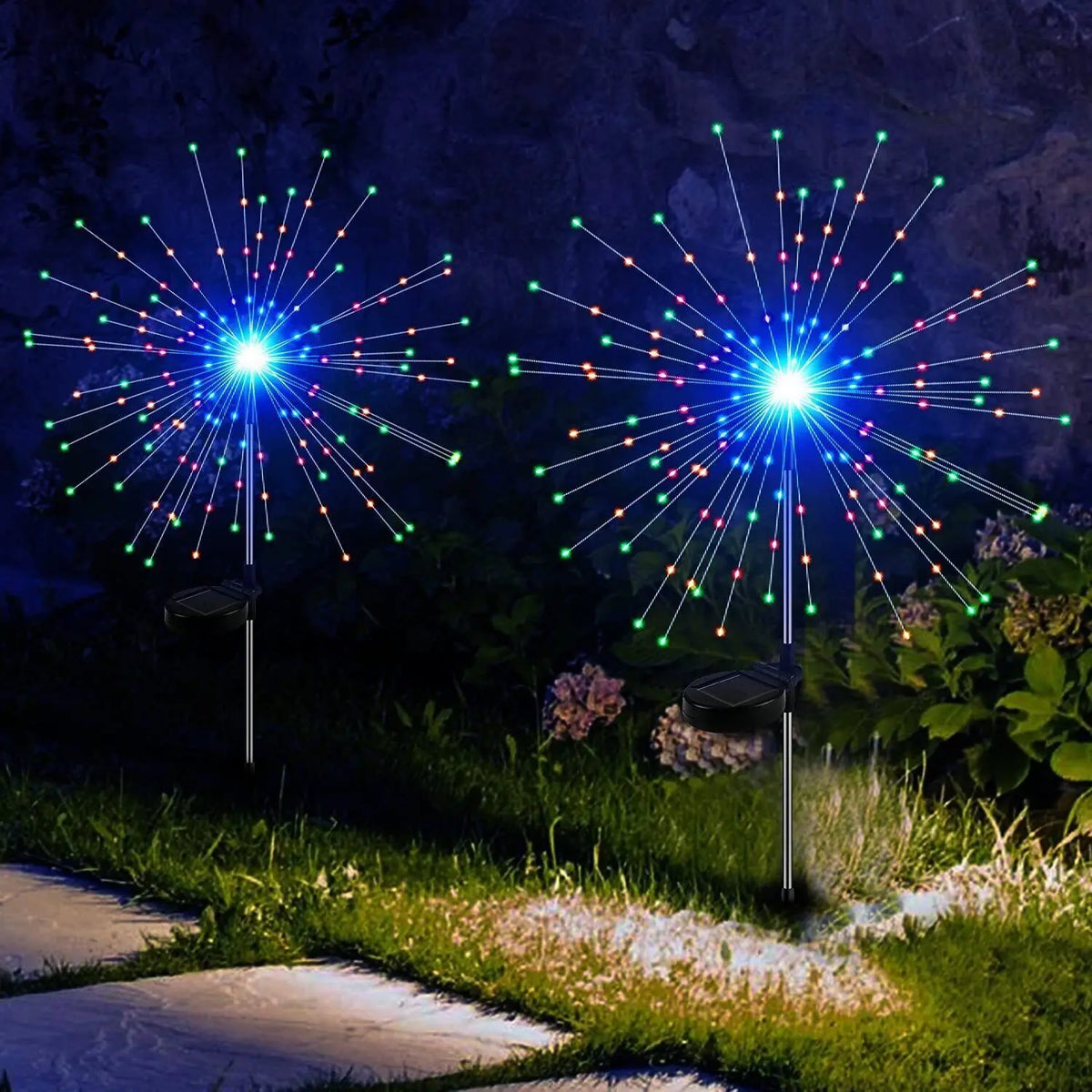 Deux feux d'artifice LED solaires verticaux, avec des traînées lumineuses bleues et vertes dans un jardin.