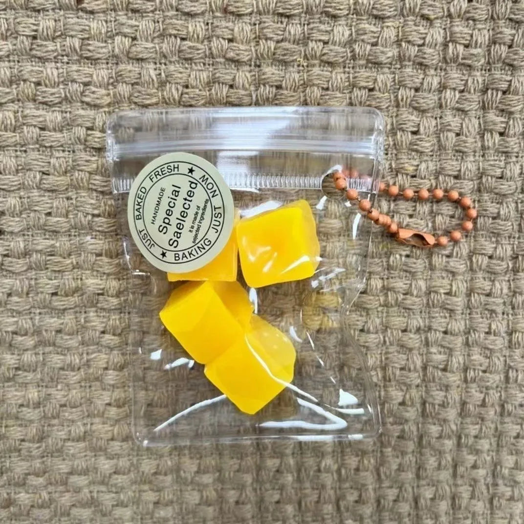 A clear plastic pouch contains several yellow, cube-shaped fruit keychains with a circular label.