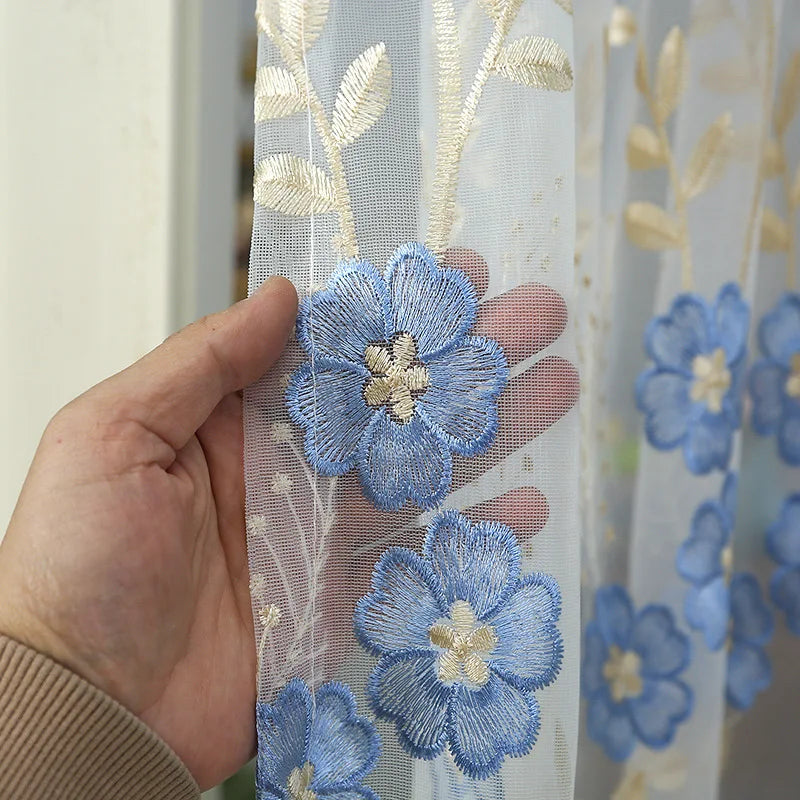Close-up of light blue embroidered sheer lace fabric featuring floral patterns and gold accents.