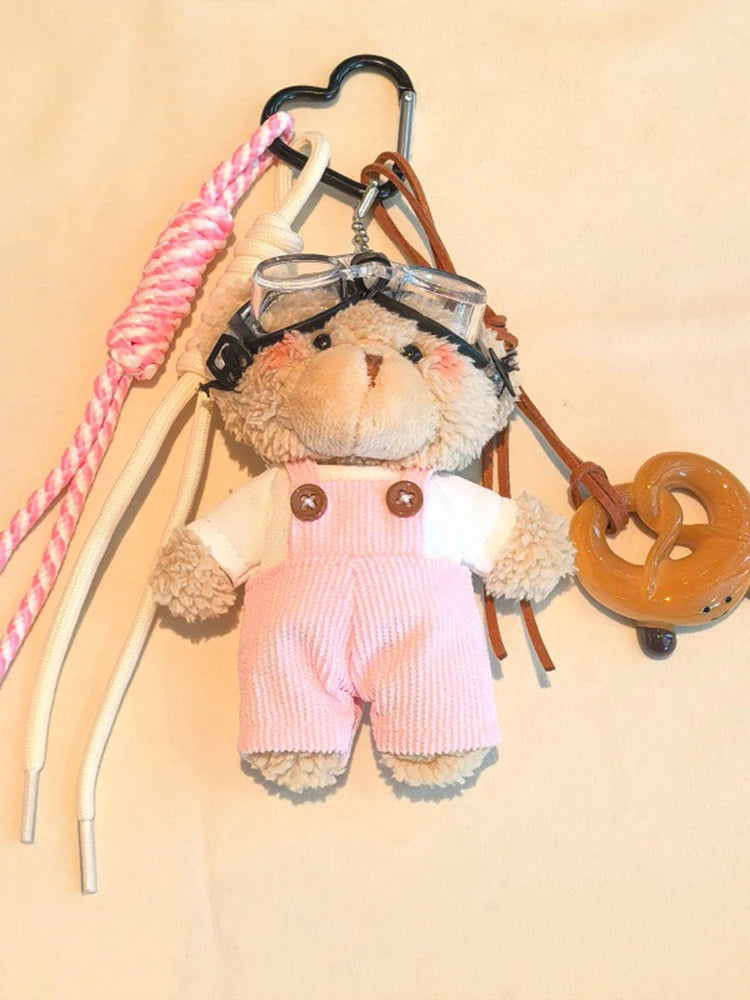 Un ours en peluche rose et duveteux portant des lunettes de pilote est attaché à une clé USB avec des sangles en cuir rose et
