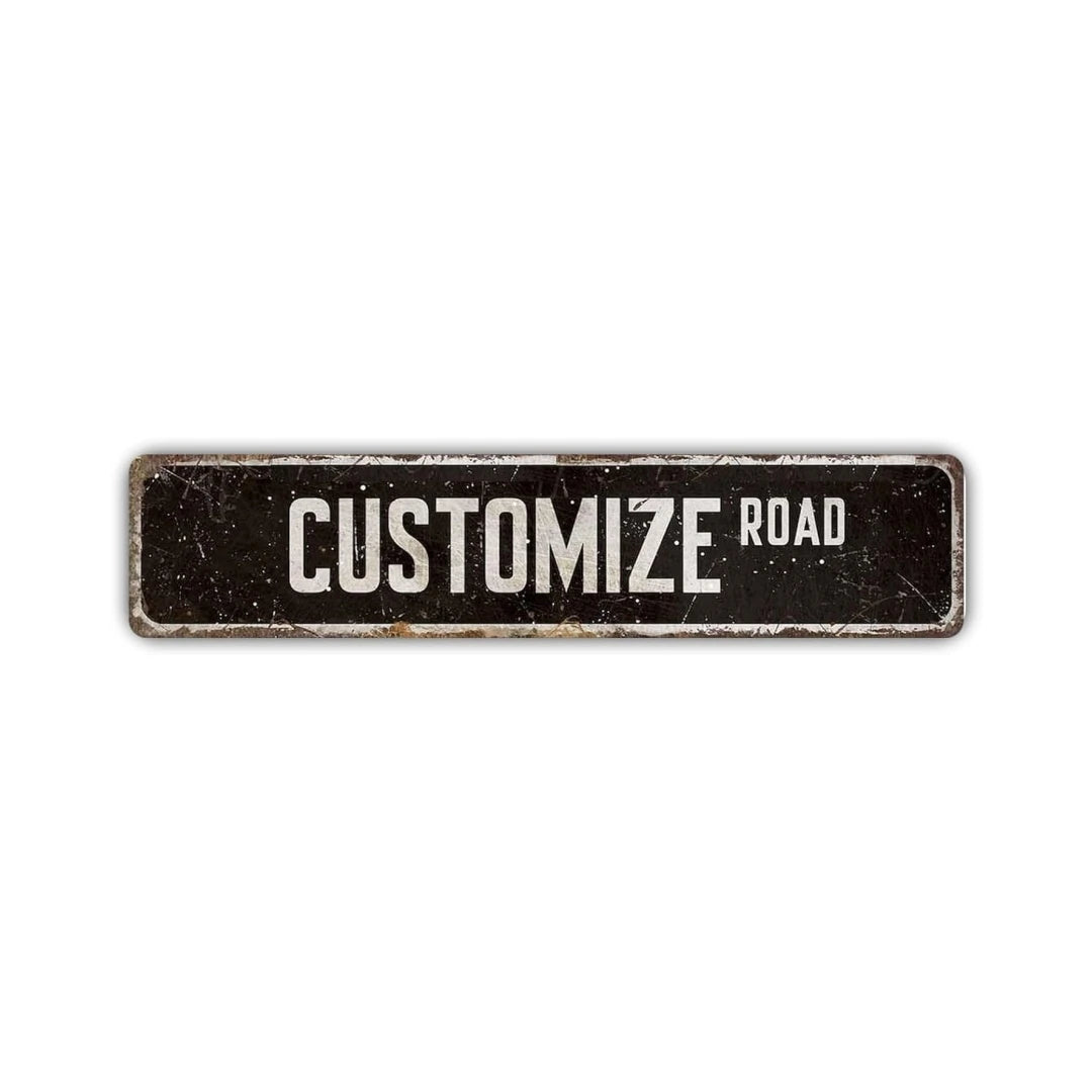 A dark rectangular aluminum street sign with the words CUSTOMIZE ROAD engraved on it.