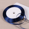A dark blue satin ribbon spool with white ribbon wrapped around it, resting on a light surface.
