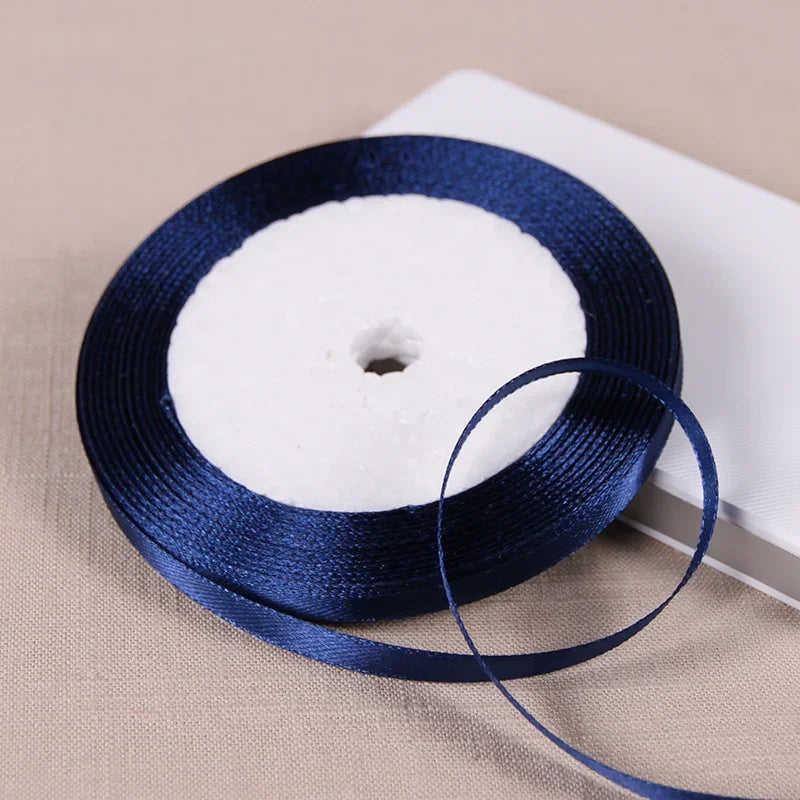 A dark blue satin ribbon spool with white ribbon wrapped around it, resting on a light surface.