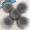 Une collection de pompons et de boules de cheveux en fausse fourrure grise exposés sur une surface blanche.
