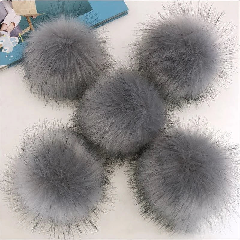 Une collection de pompons et de boules de cheveux en fausse fourrure grise exposés sur une surface blanche.