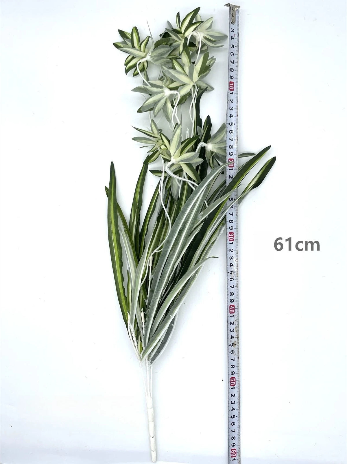 Artificial chlorophytum branch with long green leaves displayed against a measuring stick.