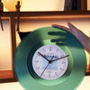 A hand holds a green vintage vinyl record wall clock with a transparent cover, showing the time.