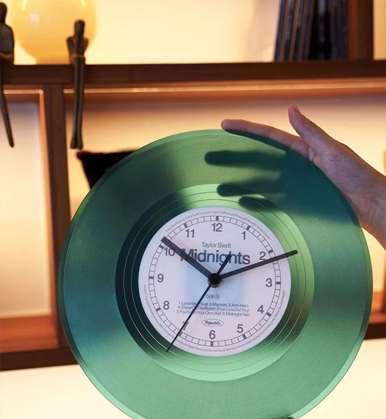 A hand holds a green vintage vinyl record wall clock with a transparent cover, showing the time.
