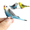 Three hand-painted resin parrot figurines, including a blue and white bird and a yellow bird, are shown being held by a hand.