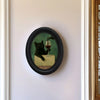 Framed wall art depicting a black cat drinking wine on a table.