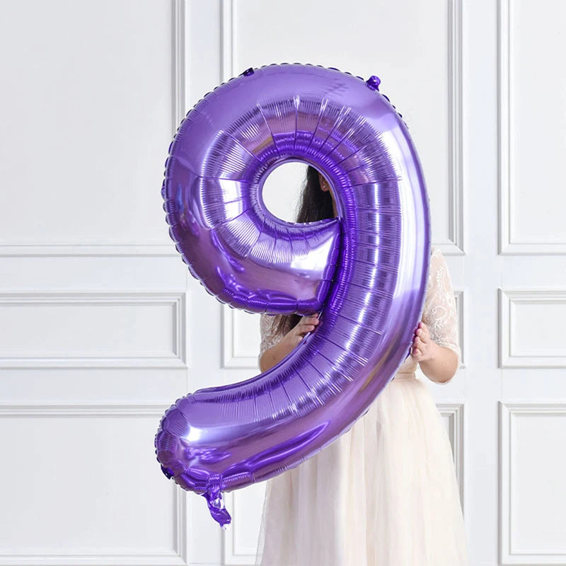 A purple foil number balloon shaped like the number 9 is held by a person against a white paneled background.