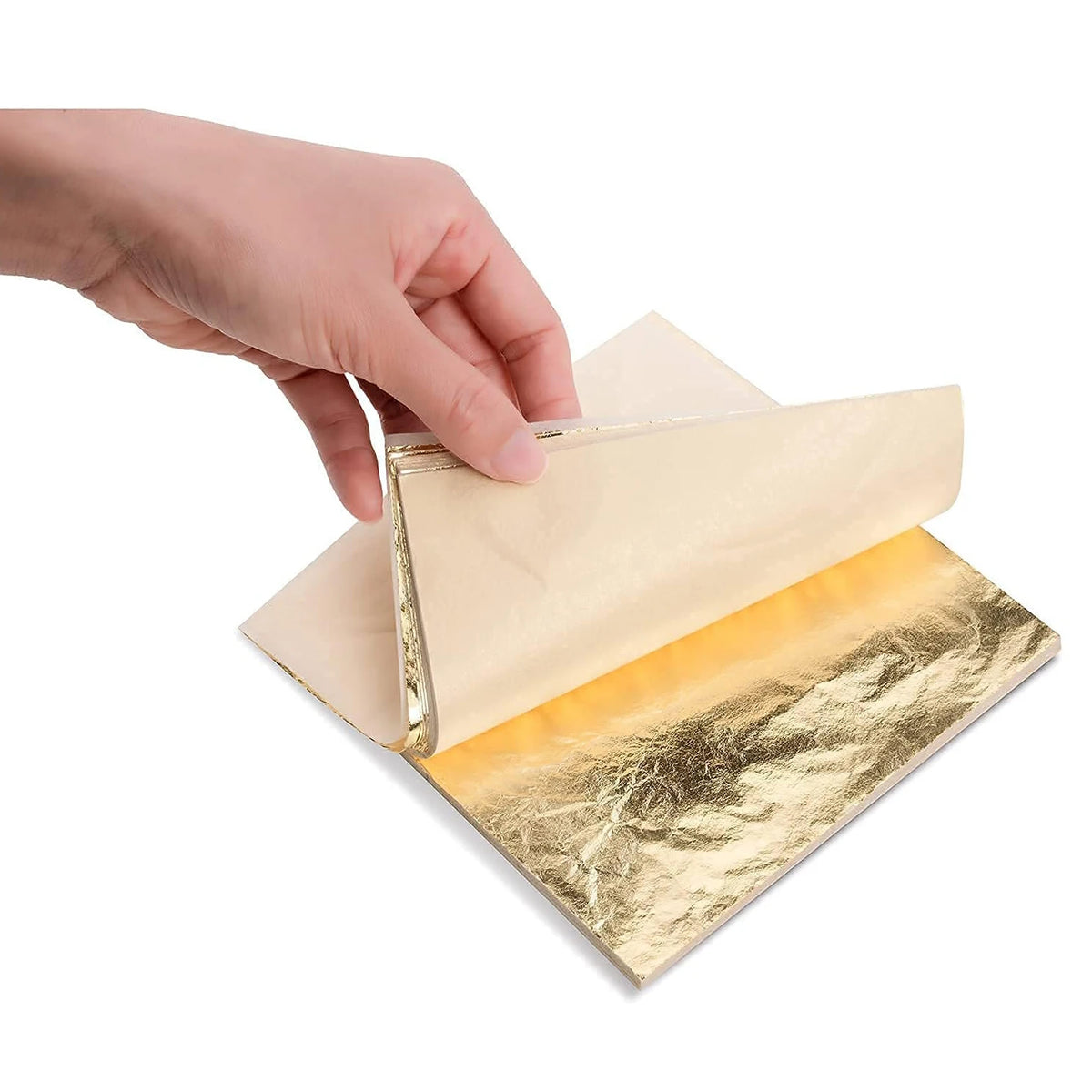 A hand is applying imitation gold leaf sheets onto a piece of paper for crafting or gilding.