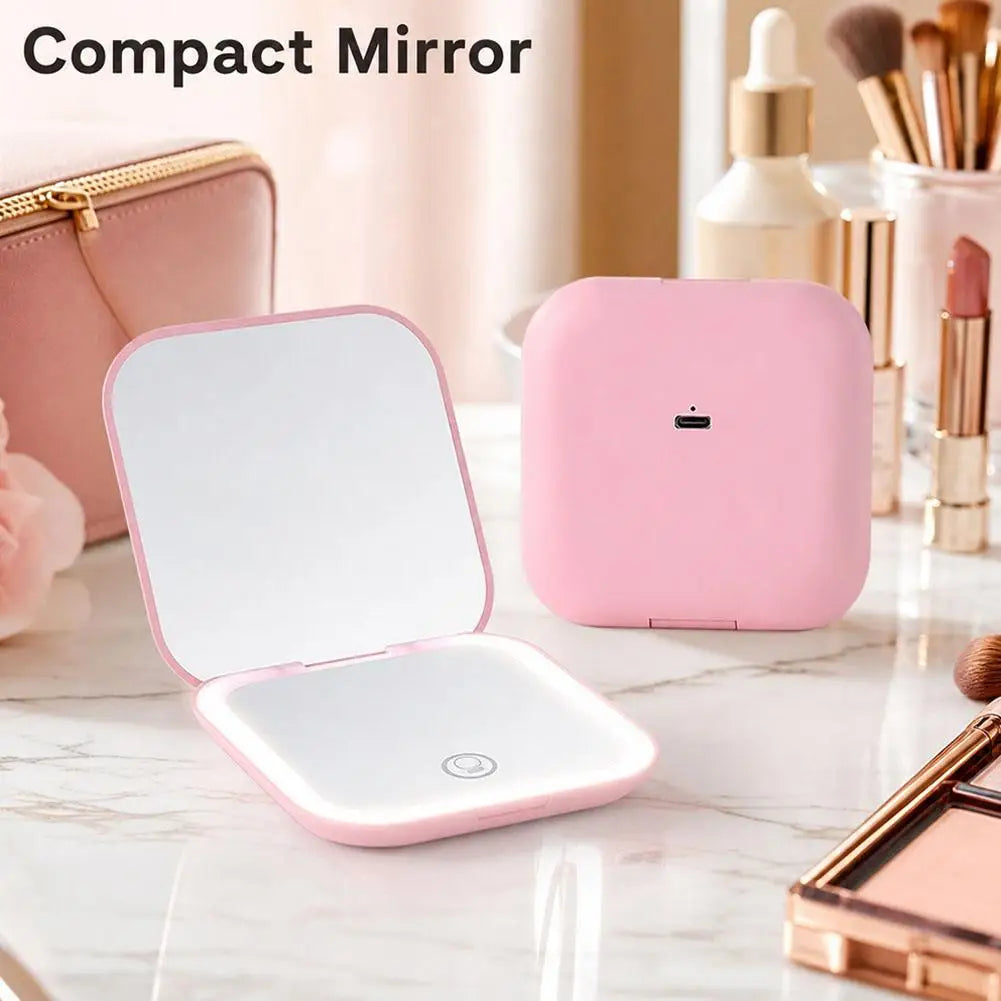 A pink portable folding LED makeup mirror is shown open on a marble surface next to various makeup brushes and cosmetic produ