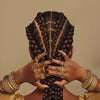 A portrait of a woman's hands intricately braided with gold jewelry, set against a neutral background.