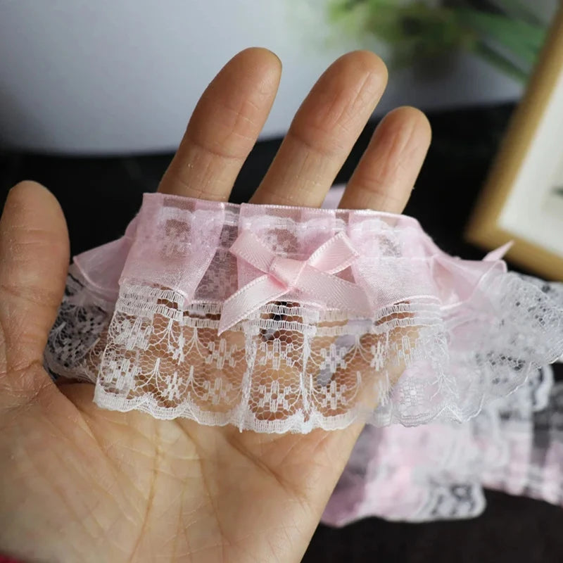 Pink lace trim with a delicate bow ruffle is held in a hand.