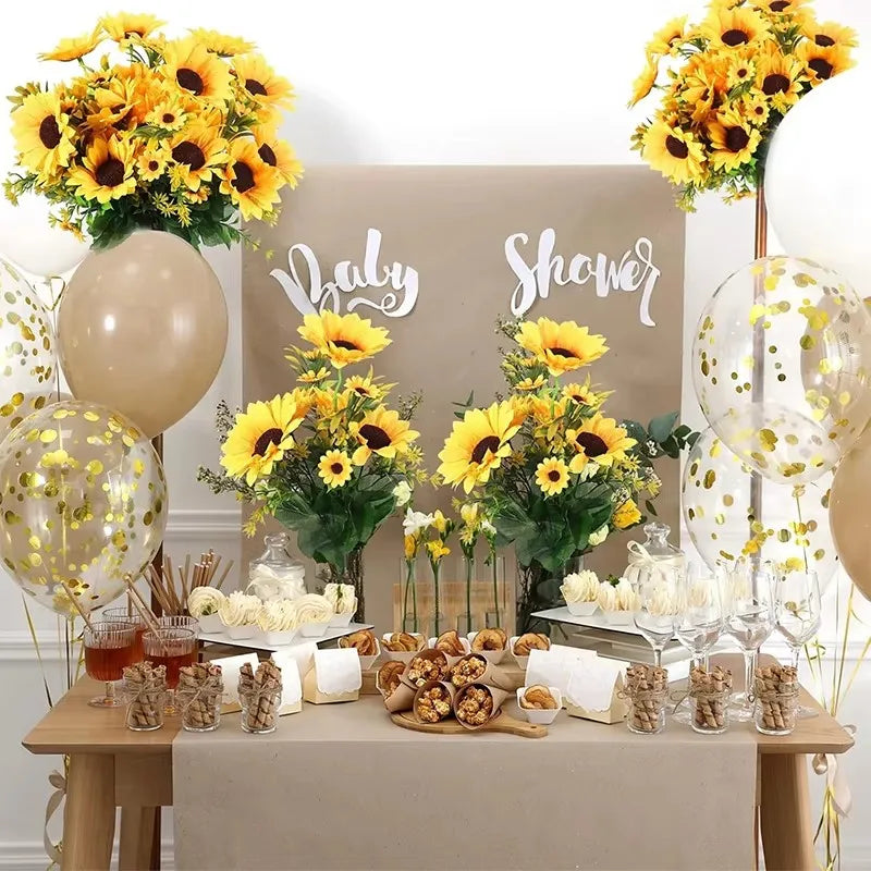 A table display featuring an artificial sunflower bouquet, balloons, and treats for a baby shower event.