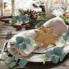 A light beige starfish decoration rests on a white plate surrounded by eucalyptus leaves.
