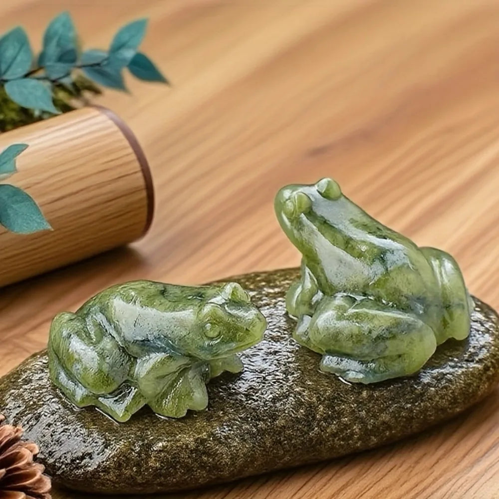 Une petite figurine de grenouille de jade vert translucide repose sur une pierre sombre et lisse.