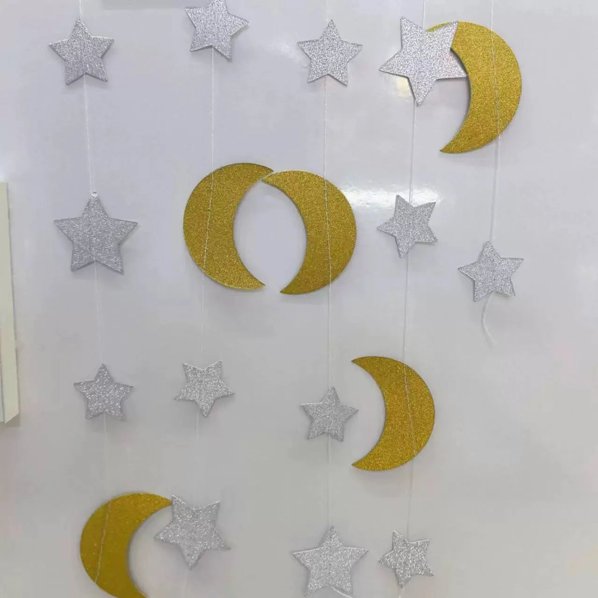 A shimmering star paper garland featuring metallic gold and silver stars and crescent moons hanging vertically.