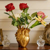 A bouquet of red and pink roses in a heart-shaped gold resin vase with glass accents.