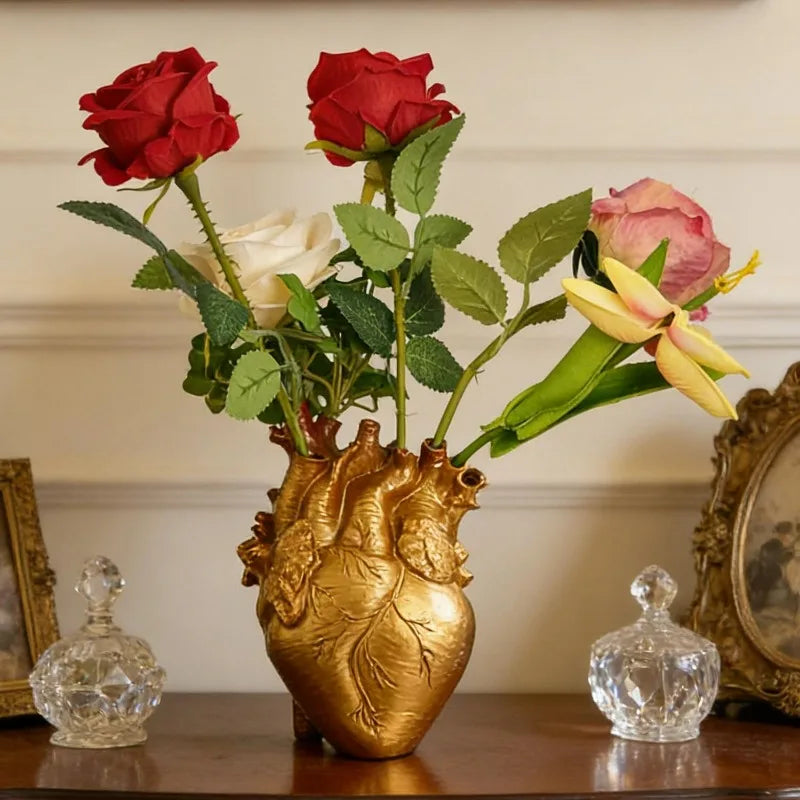 A bouquet of red and pink roses in a heart-shaped gold resin vase with glass accents.