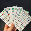 A hand holds several sheets of glitter gem stick-on facial tattoos in various colors and shapes.