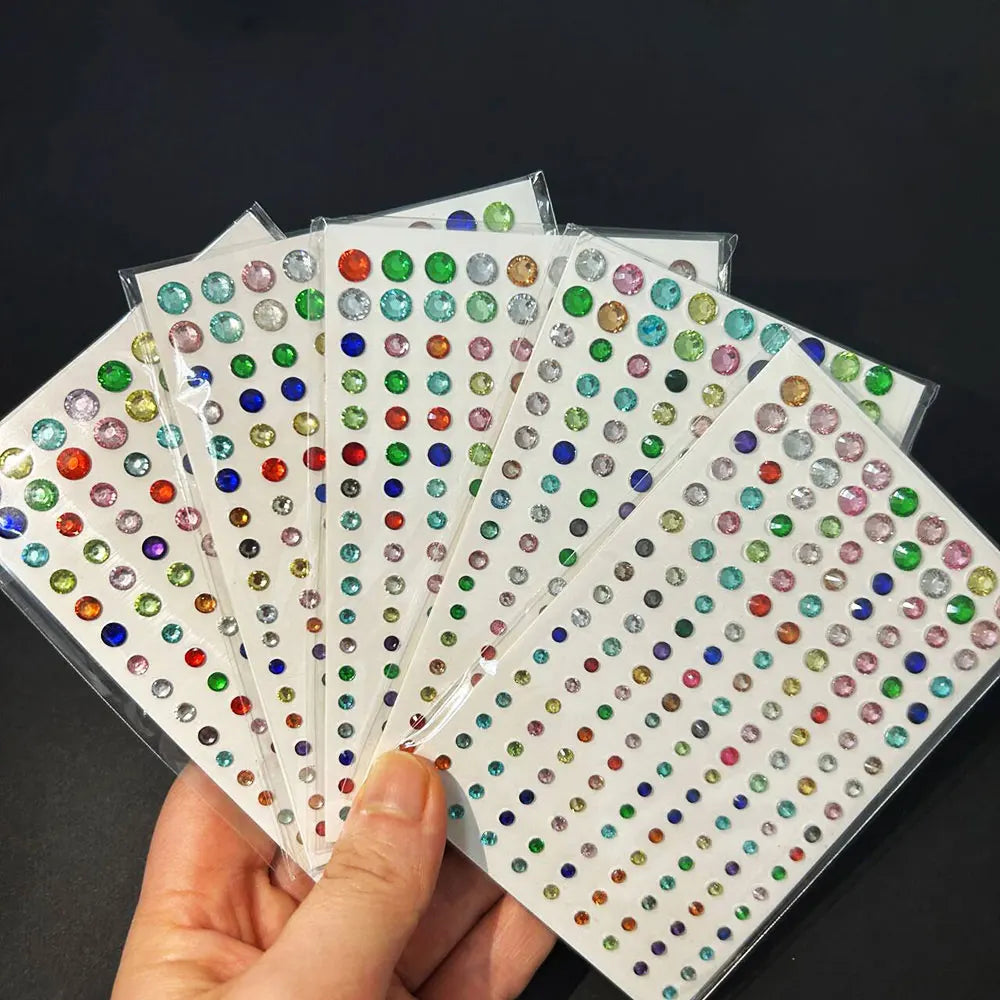 A hand holds several sheets of glitter gem stick-on facial tattoos in various colors and shapes.