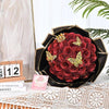 A bouquet of deep red glitter artificial roses displayed in a black decorative bowl on a white surface.