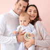 A smiling mother and father holding a baby, with a wooden sign indicating six months.