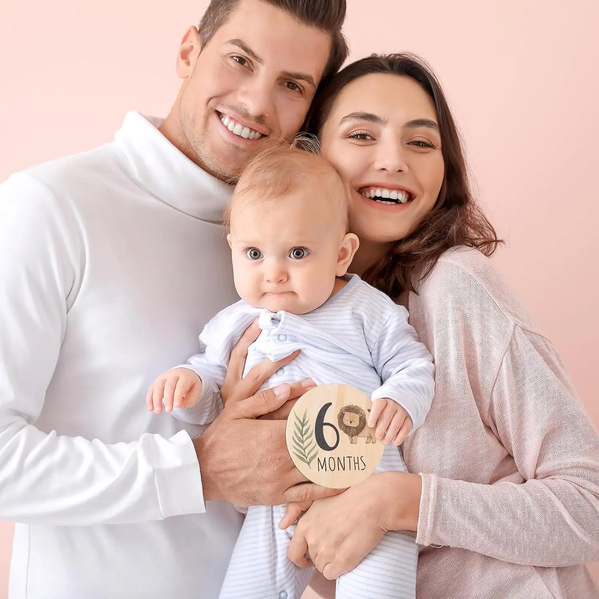 A smiling mother and father holding a baby, with a wooden sign indicating six months.