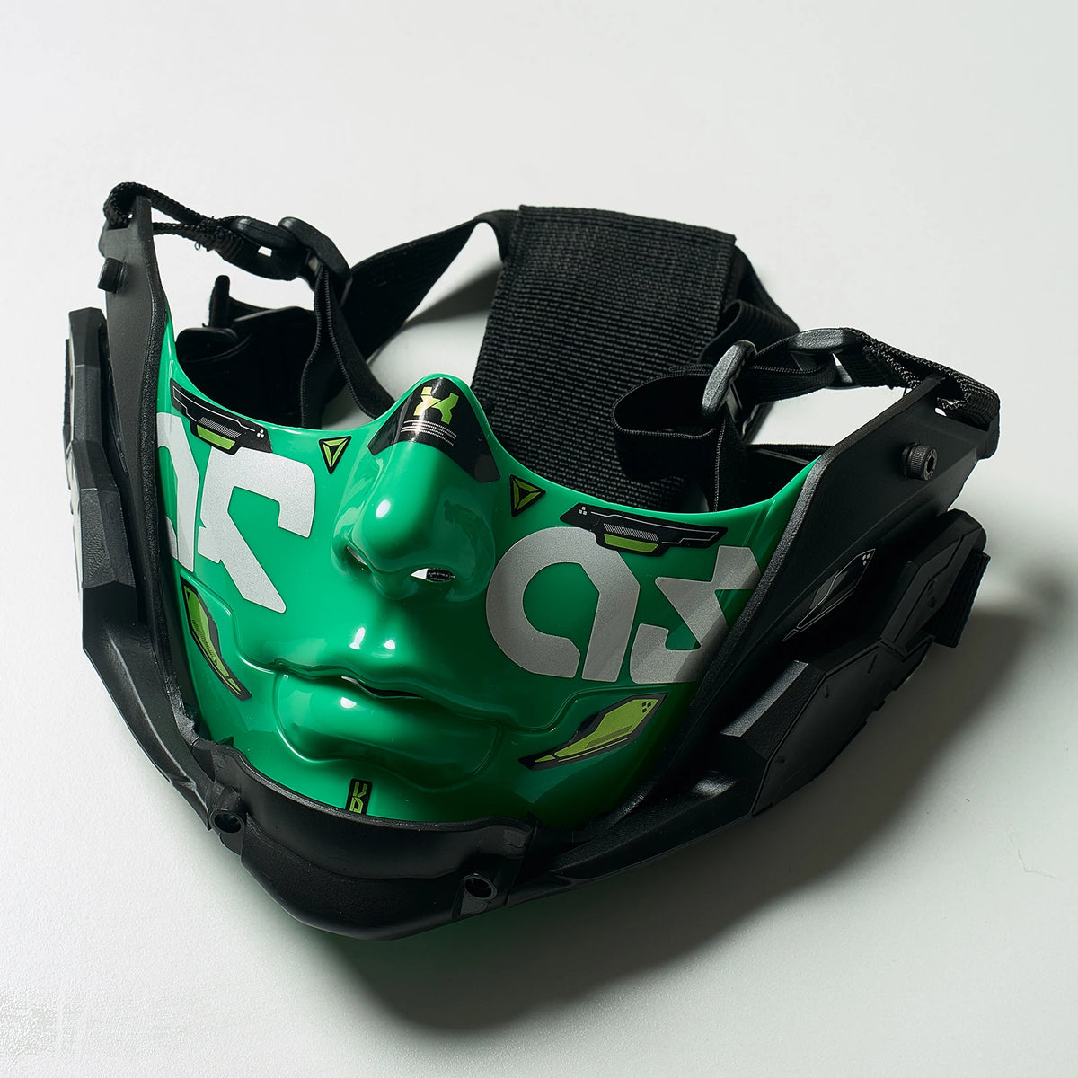 A green cyberpunk half face mask with black straps is shown against a white background.