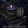 A dark, moody photograph of a High Priestess tarot candle with crystal stones, set against a backdrop of dark foliage and a f