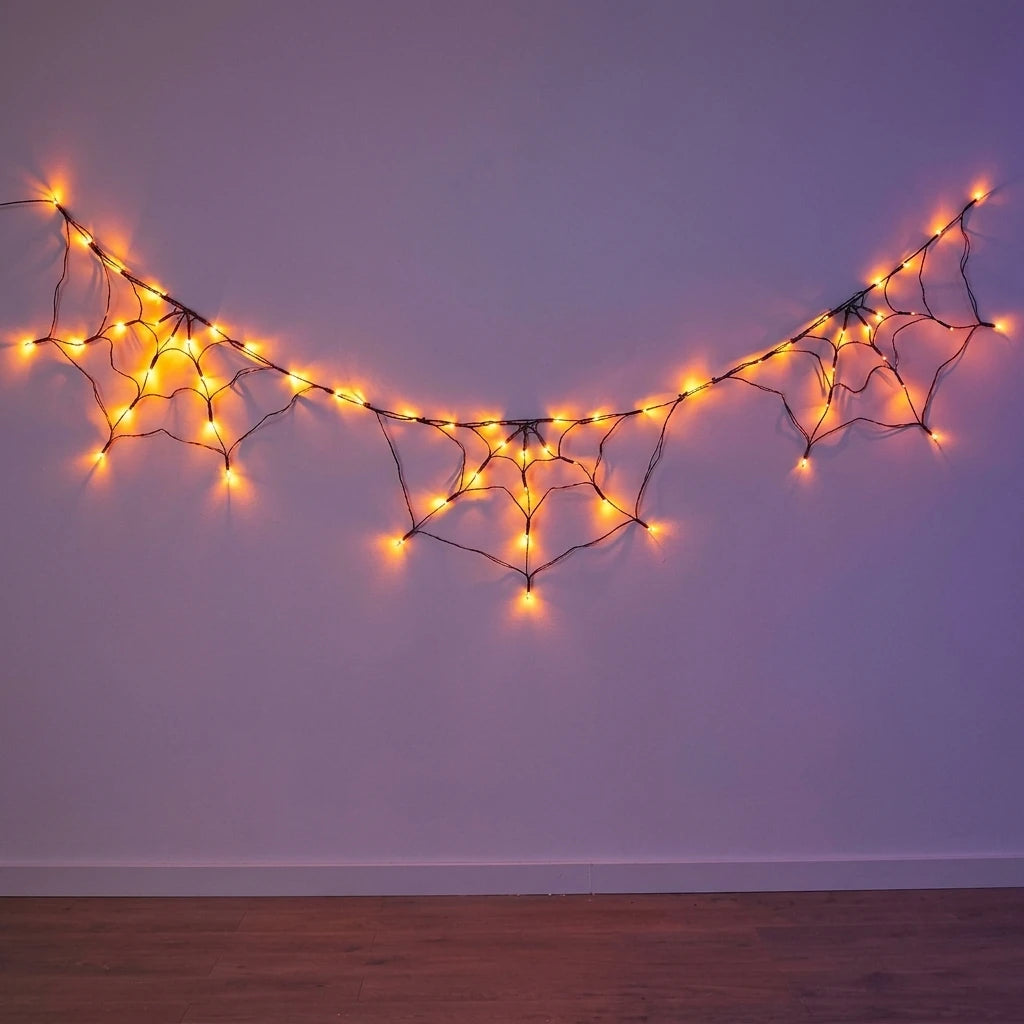 String lights shaped like spider webs illuminate a purple wall for Halloween decor.