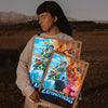 A person holds up a framed piece of digital art featuring dynamic fantasy scenes and the text Minecraft Legends