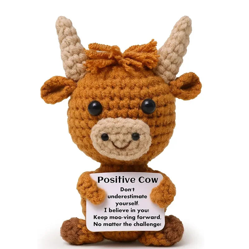 A handcrafted crochet cow doll with brown fur and black eyes, featuring a positive message card.