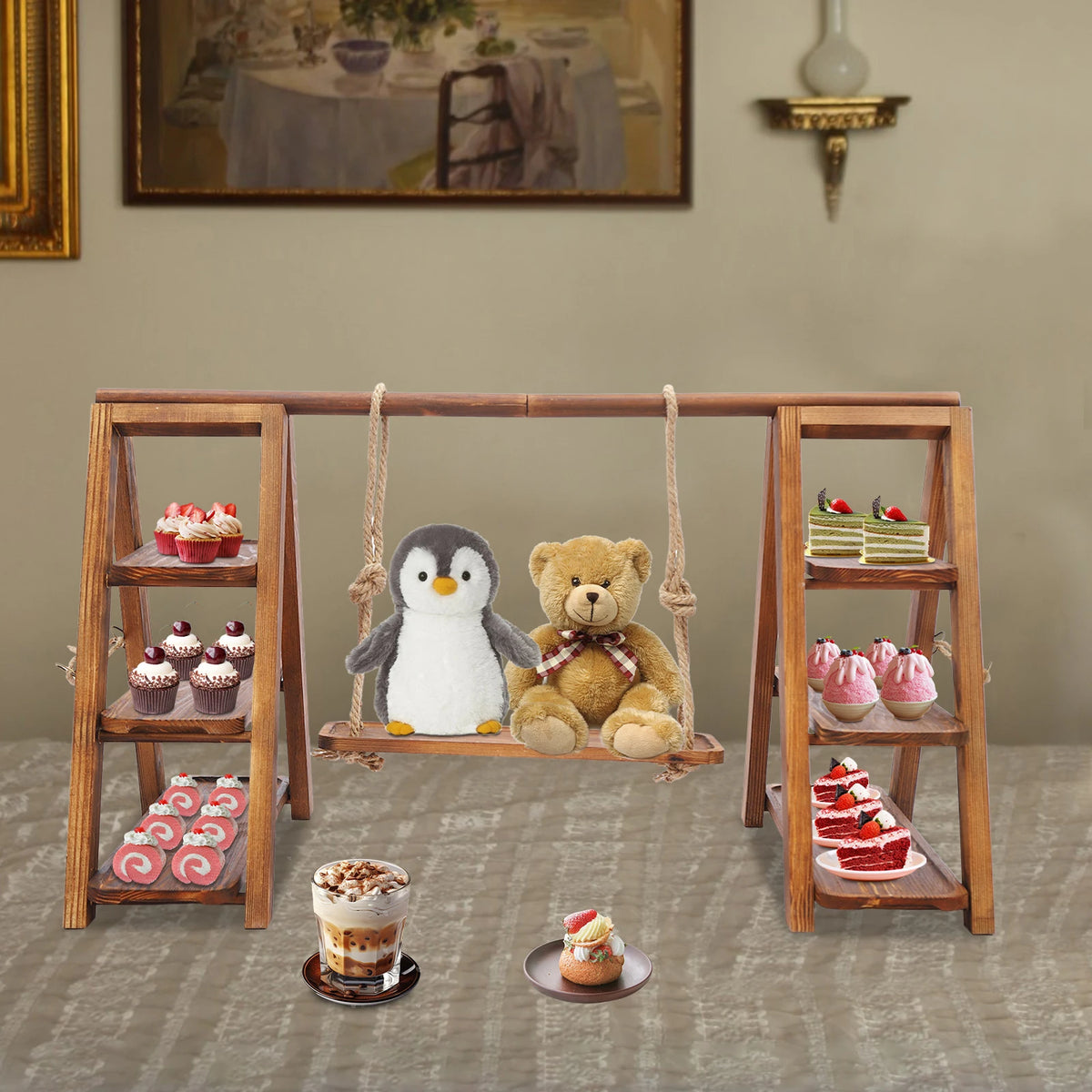 A wooden dessert display stand featuring a hanging bear and penguin, holding various small cakes and desserts.