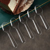 Five clear plastic disposable spoons arranged diagonally on a dark surface next to a slice of cake.