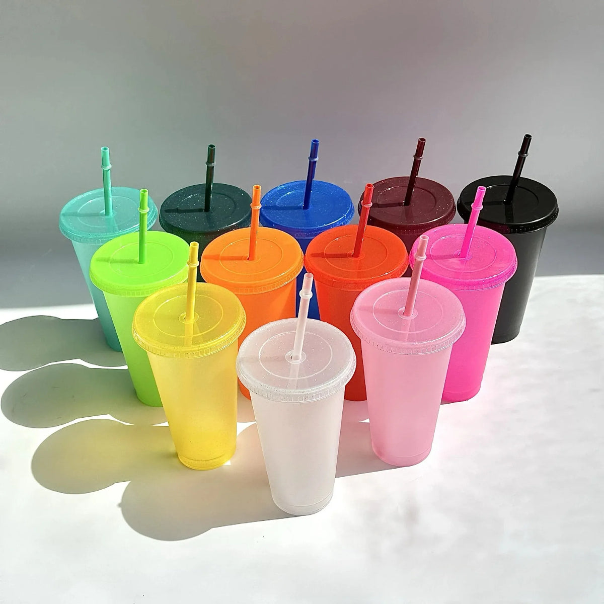 A collection of colorful glitter party cups with lids and straws arranged in a row against a white background.