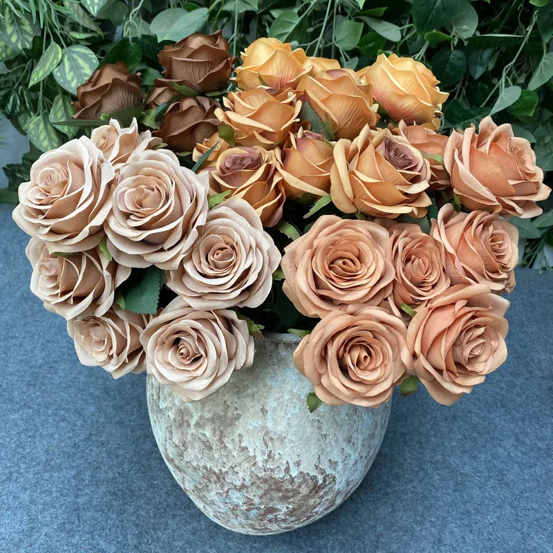 A bouquet of nine realistic silk roses in shades of peach and apricot arranged in a textured gray vase.