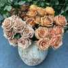 A bouquet of nine realistic silk roses in shades of peach and beige arranged in a textured gray vase.