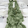 A sage green semi-sheer gauze table runner draped down a white tablecloth with place settings.