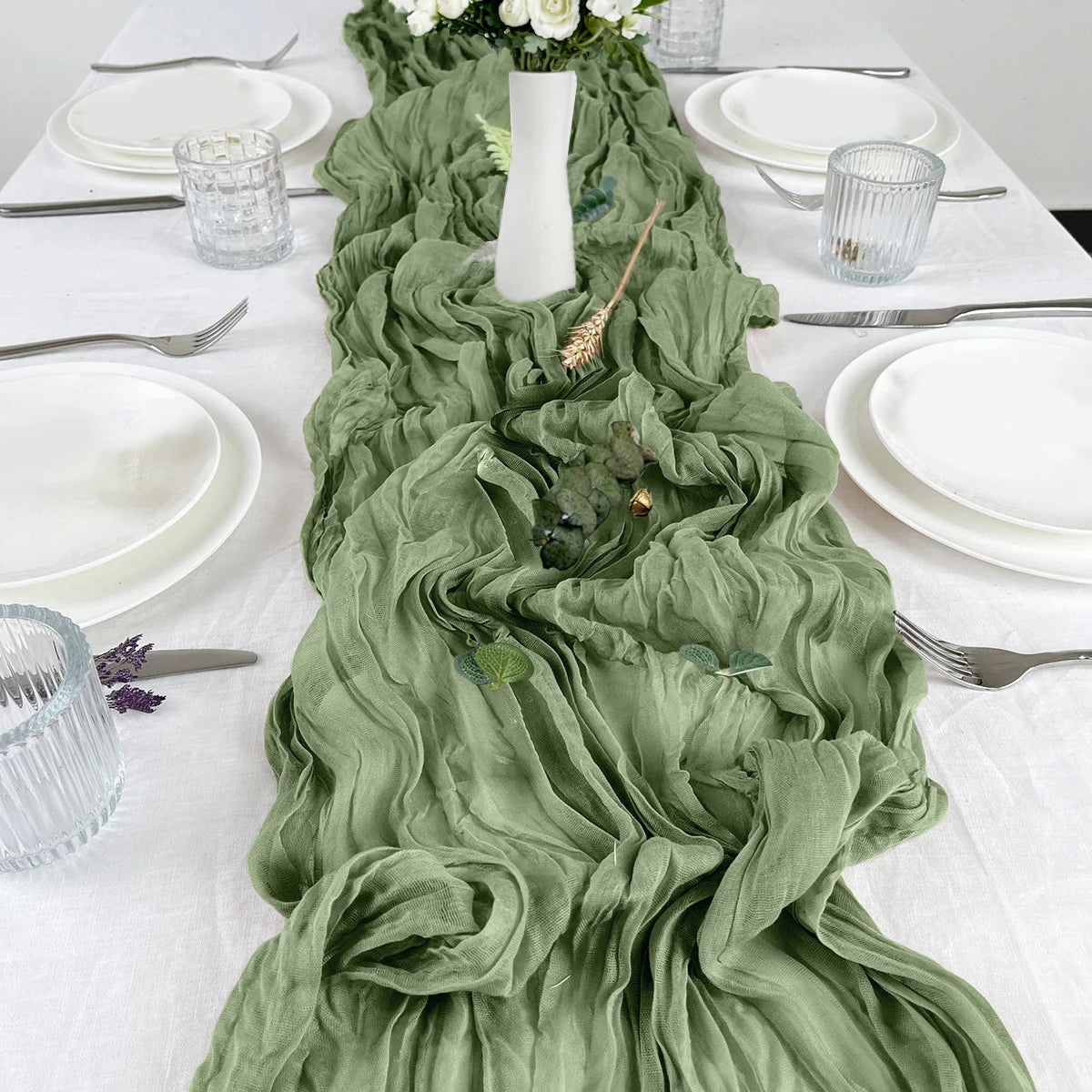 A sage green semi-sheer gauze table runner draped down a white tablecloth with place settings.