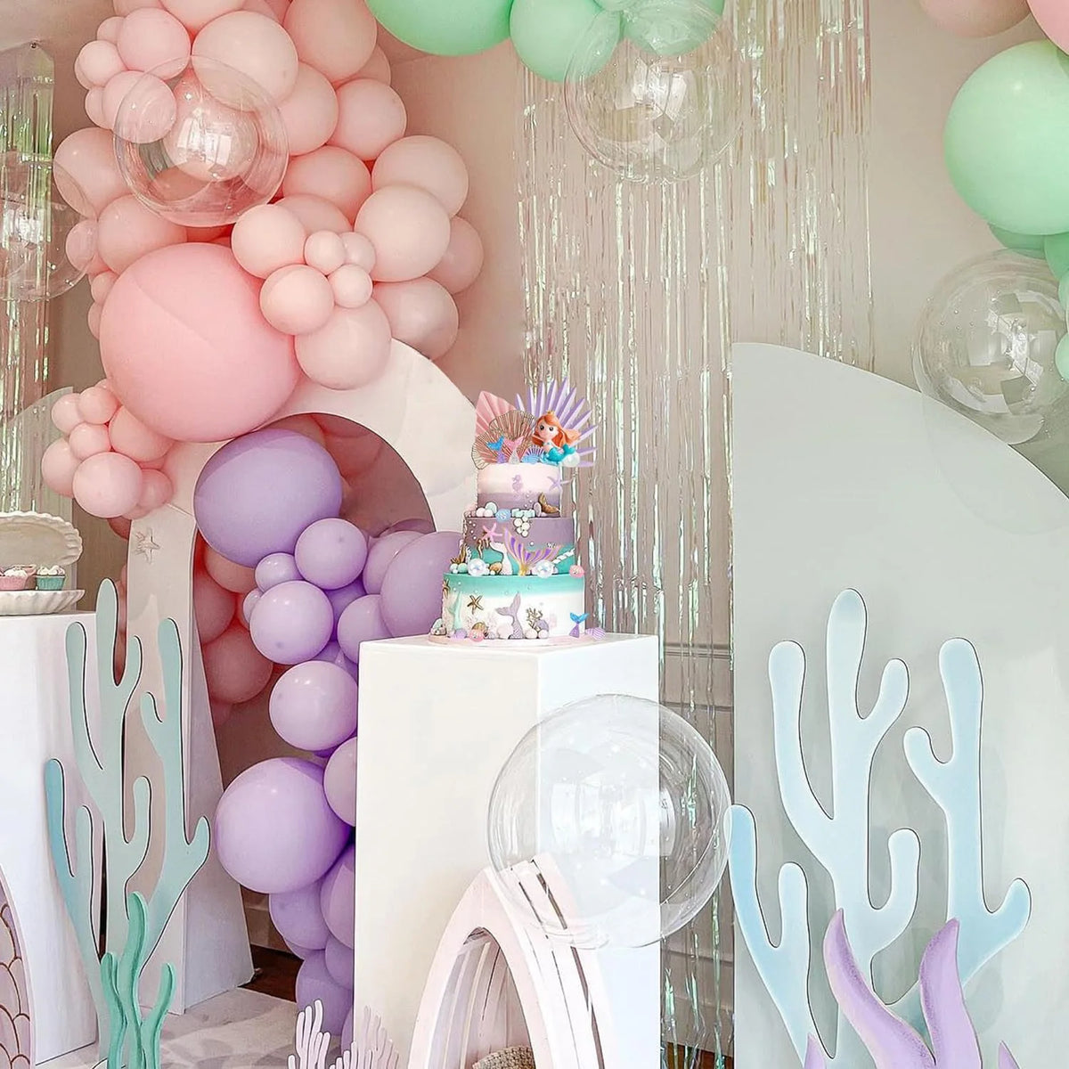 A pink and purple mermaid cake topper set featuring sea elements like shells, seaweed, and colorful balloons.