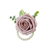 A soft pink rose corsage flower with green foliage attached to a pearl beaded bracelet.