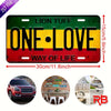 A rectangular metal wall sign featuring the text ONE LOVE in yellow on a black background with red and green stripes.